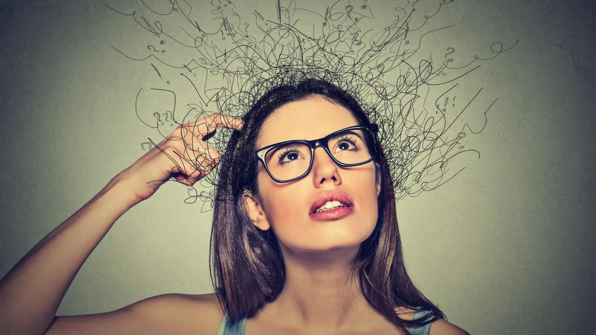 Closeup portrait young woman scratching head, thinking daydreaming with brain melting into lines question marks looking up isolated on gray background. Human facial expressions, emotion feeling sign