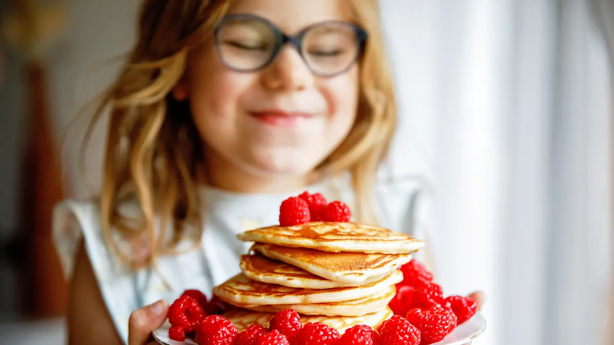 Ein glückliches Mädchen, das sich über seinen Teller mit Pfannkuchen und Himbeeren freut.