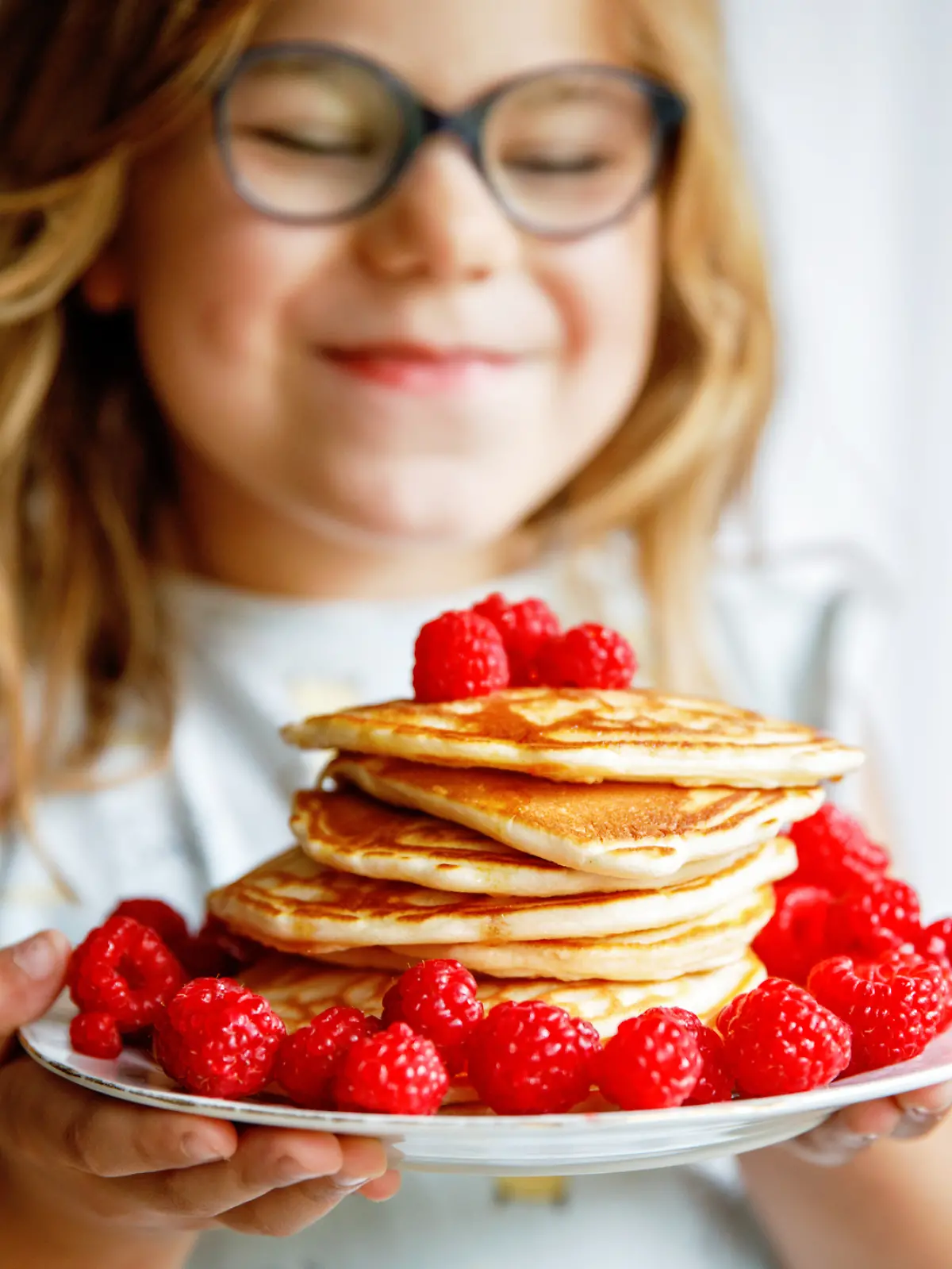 Ein glückliches Mädchen, das sich über seinen Teller mit Pfannkuchen und Himbeeren freut.