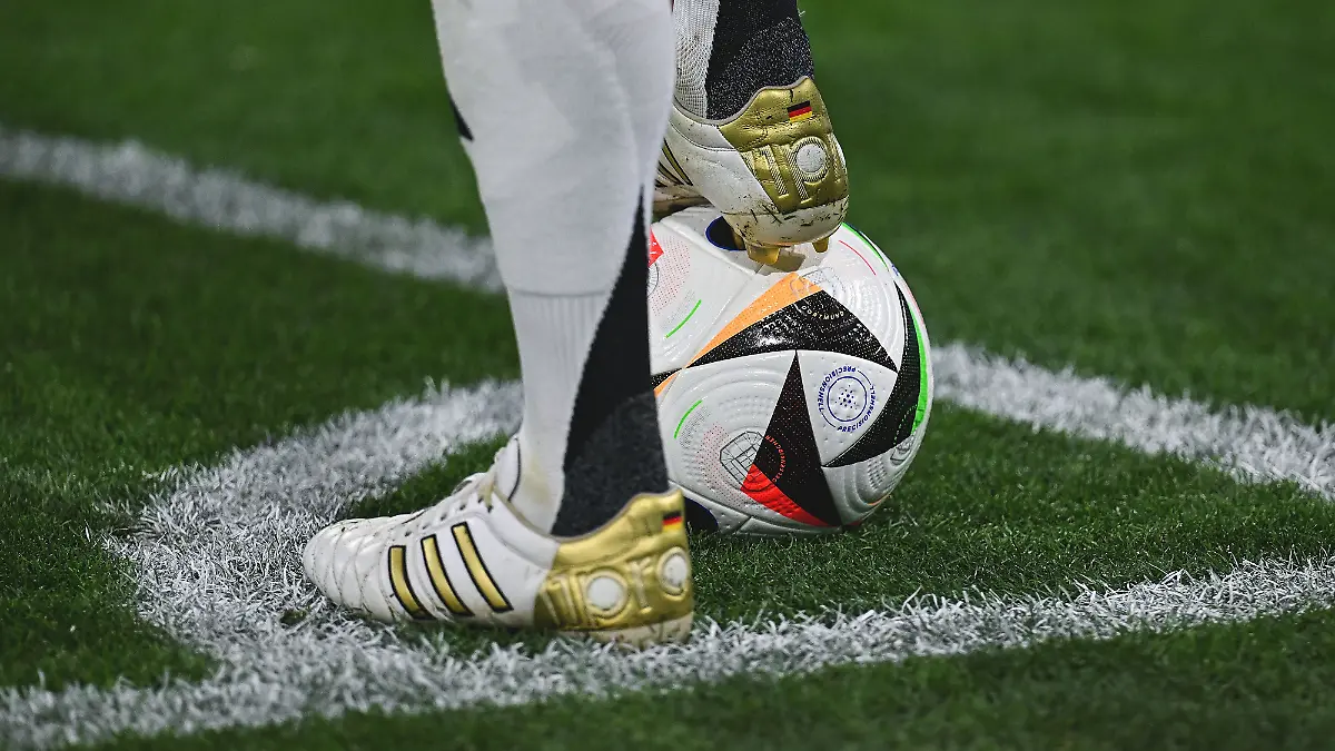 Die weißen Fußball-Schuhe mit goldenen Applikationen von Toni Kroos: Der Fußball-Nationalspieler steht mit einem Fuß auf einem Fußball, der andere Fuß daneben