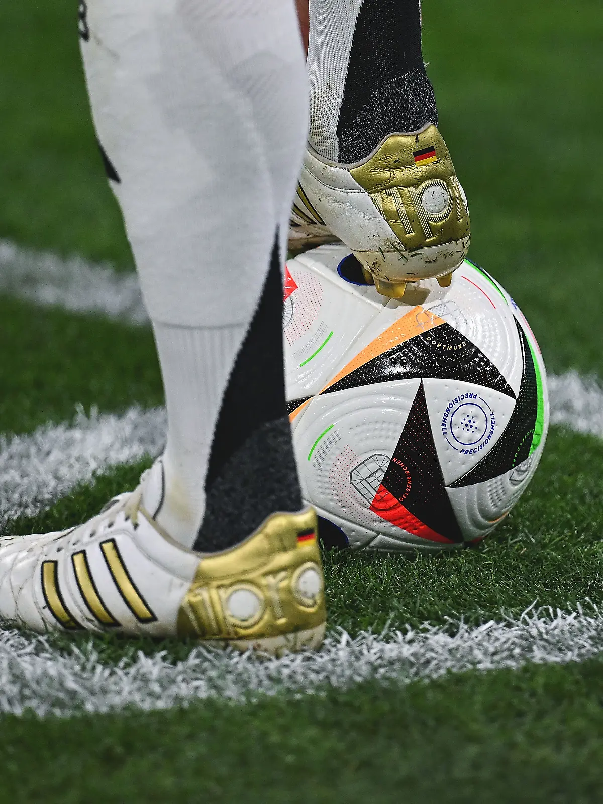 Die weißen Fußball-Schuhe mit goldenen Applikationen von Toni Kroos: Der Fußball-Nationalspieler steht mit einem Fuß auf einem Fußball, der andere Fuß daneben