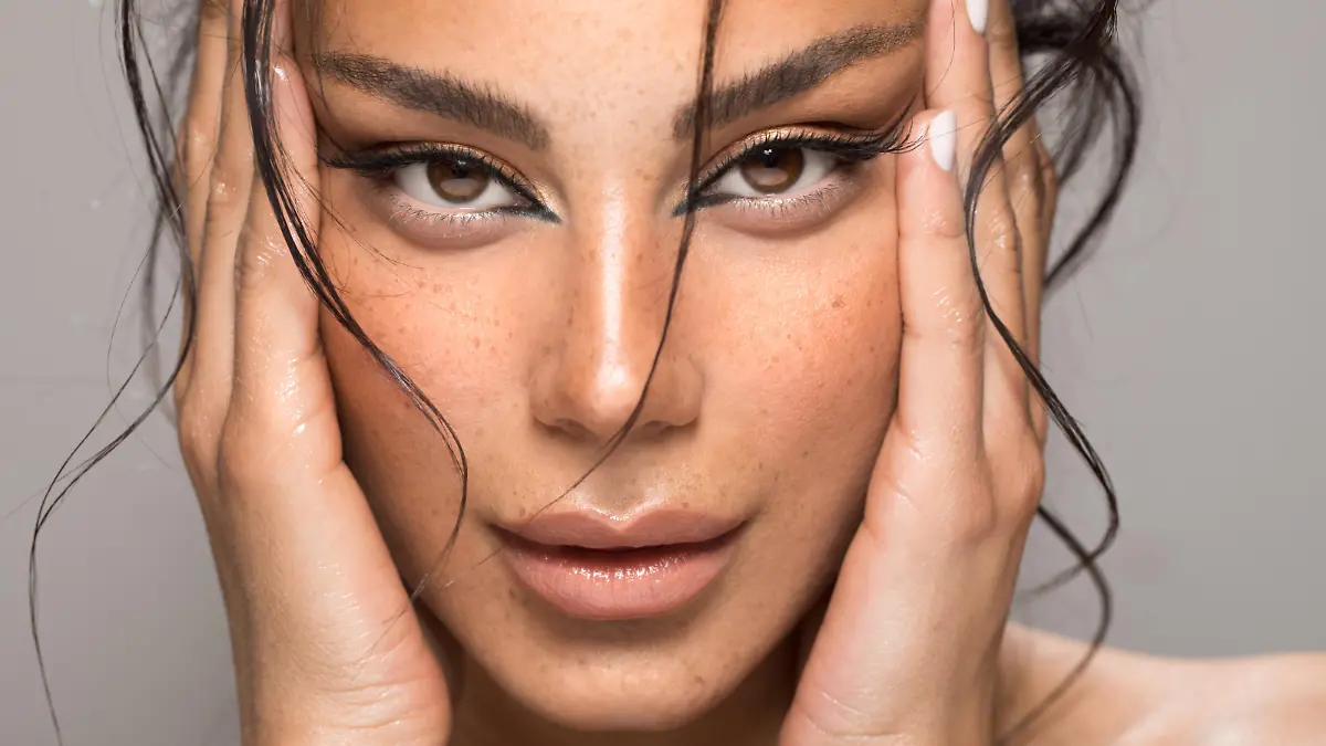 Close up studio shot of a beautiful brunette woman with glowing skin. Holding hands near her face.