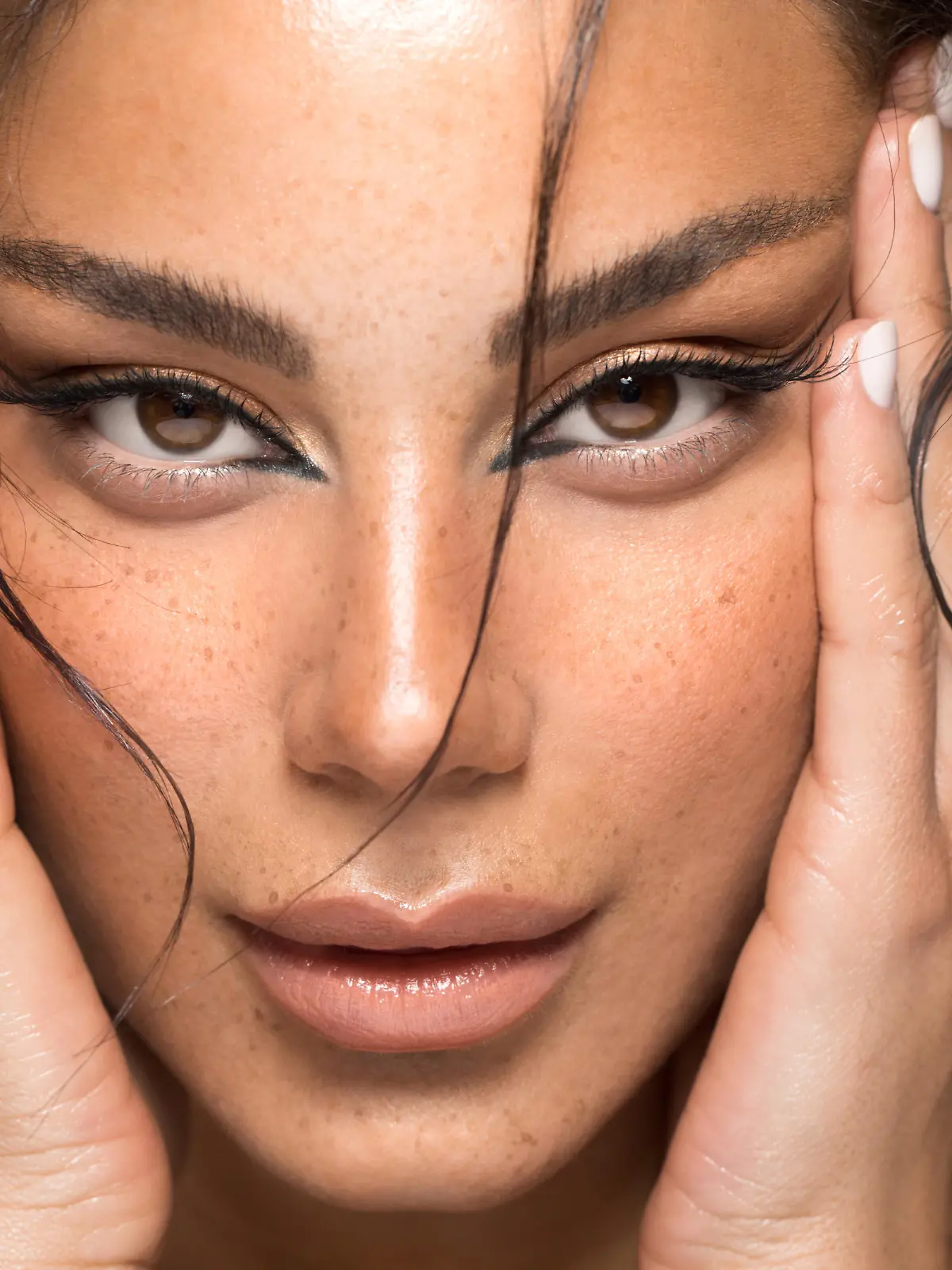 Close up studio shot of a beautiful brunette woman with glowing skin. Holding hands near her face.