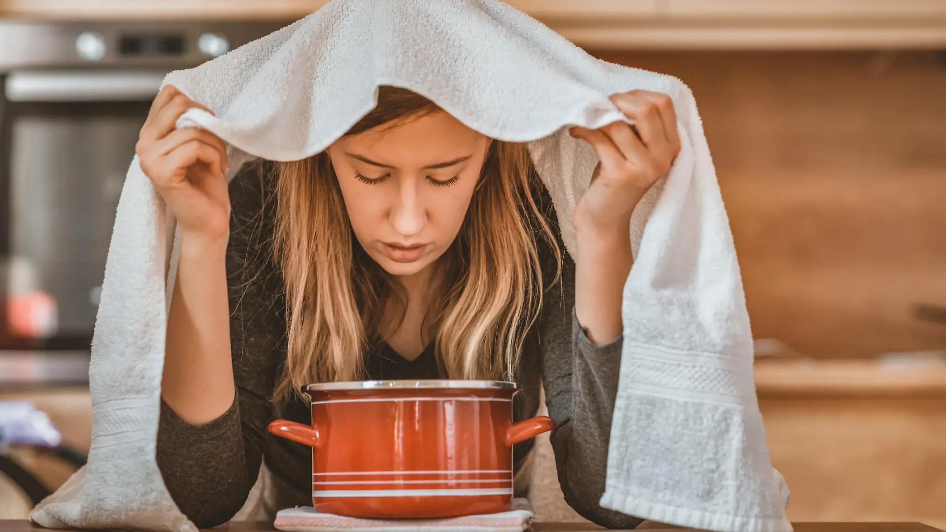 Health care, flu, hygiene and people concept - Photo of sick brown hair woman at home inhaling over a bowl. Rhinitis treatment at home by inhalation. Young woman inhaling chamomile tea steam as an alternative therapy or traditional cure. Young woman inhales steam to treat a blocked nose during the day.