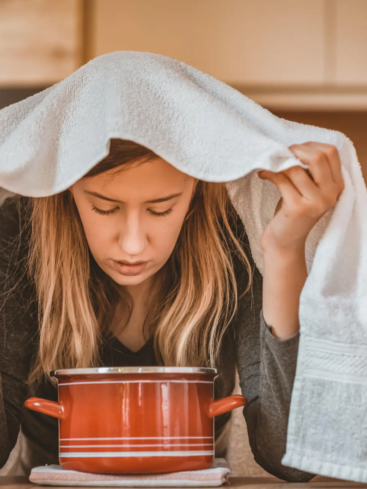 Health care, flu, hygiene and people concept - Photo of sick brown hair woman at home inhaling over a bowl. Rhinitis treatment at home by inhalation. Young woman inhaling chamomile tea steam as an alternative therapy or traditional cure. Young woman inhales steam to treat a blocked nose during the day.