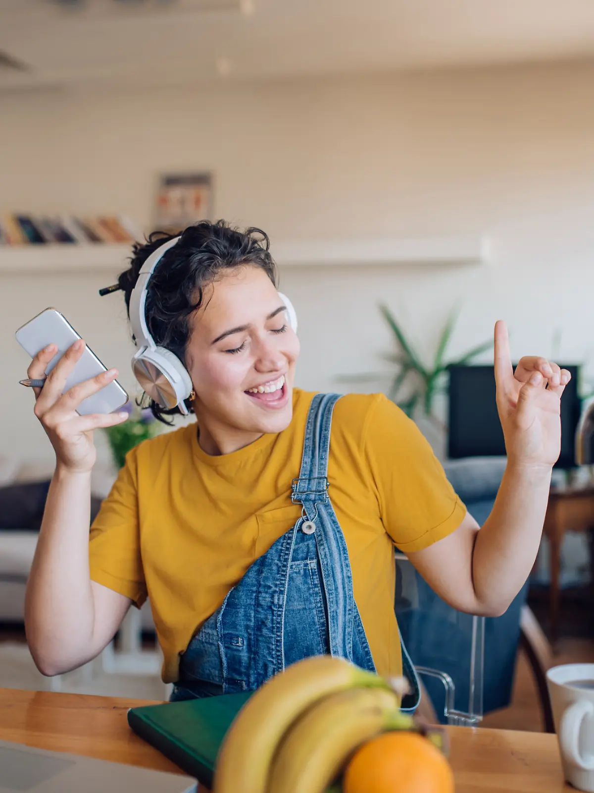 Eine junge Frau hört mit Kopfhörern Musik und ist gut gelaunt.