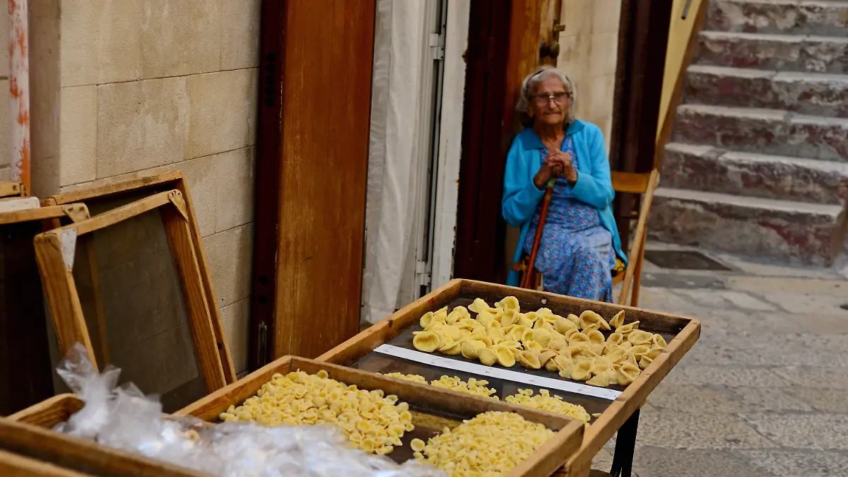 Symbolbild Reise / Urlaub / Italien Eine Gasse im Zentrum der apulischen Hauptstadt Bari in Italien. Eine von viele Damen stellen die aus Apulien stammenden Orecchiette, zu Deutsch „Öhrchen” in Handarbeit her. Zum Trocknen auf Gitter gelegt, säumen die Nudeln auf Tischen die Gassen in Bari.