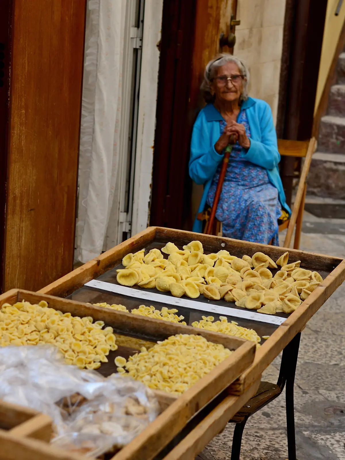 Symbolbild Reise / Urlaub / Italien Eine Gasse im Zentrum der apulischen Hauptstadt Bari in Italien. Eine von viele Damen stellen die aus Apulien stammenden Orecchiette, zu Deutsch „Öhrchen” in Handarbeit her. Zum Trocknen auf Gitter gelegt, säumen die Nudeln auf Tischen die Gassen in Bari.