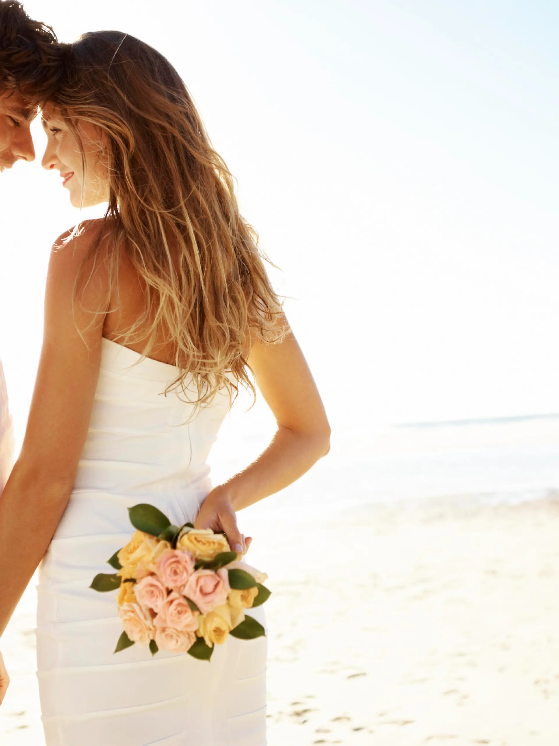 A young couple standing head-to-head on the beach while the woman holds flowers