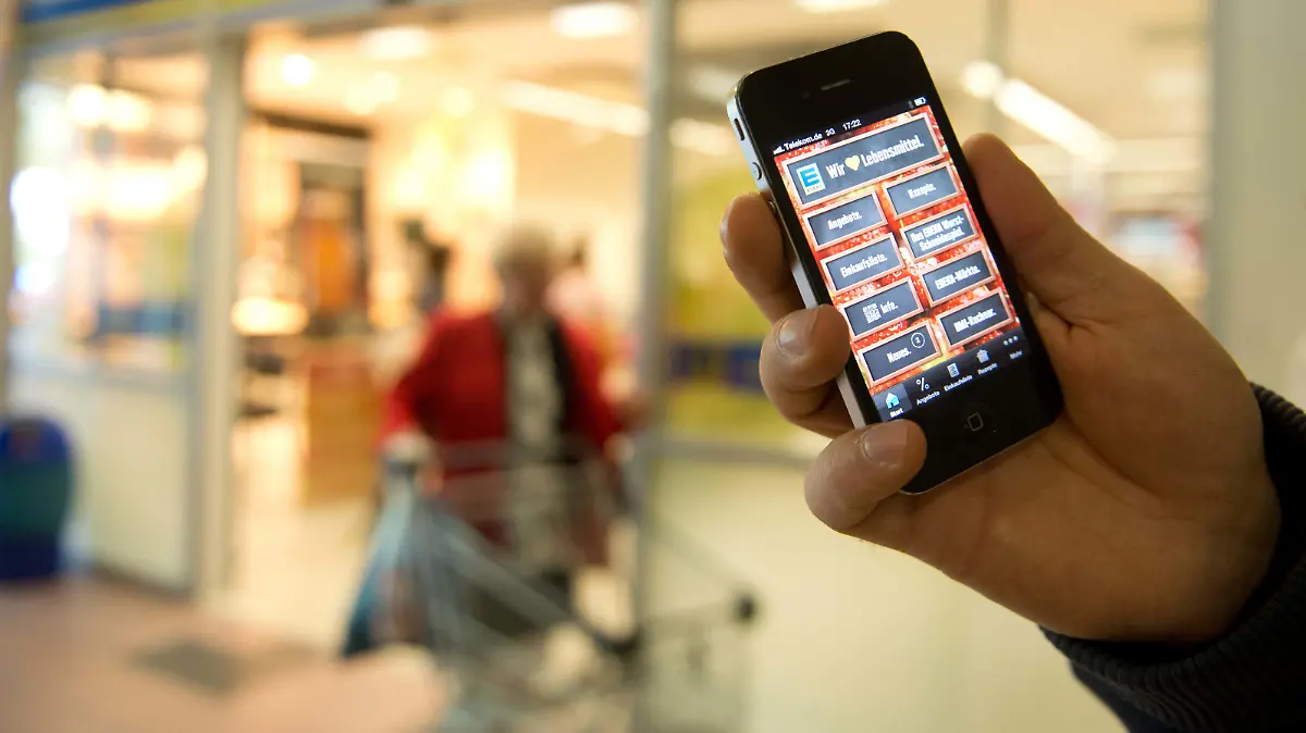 ILLUSTRATION - Ein Passant hält am 27.05.2013 in Berlin vor einem Edeka-Supermarkt ein Telefon mit der Edeka-App in die Kamera. Foto: Joanna Scheffel/dpa