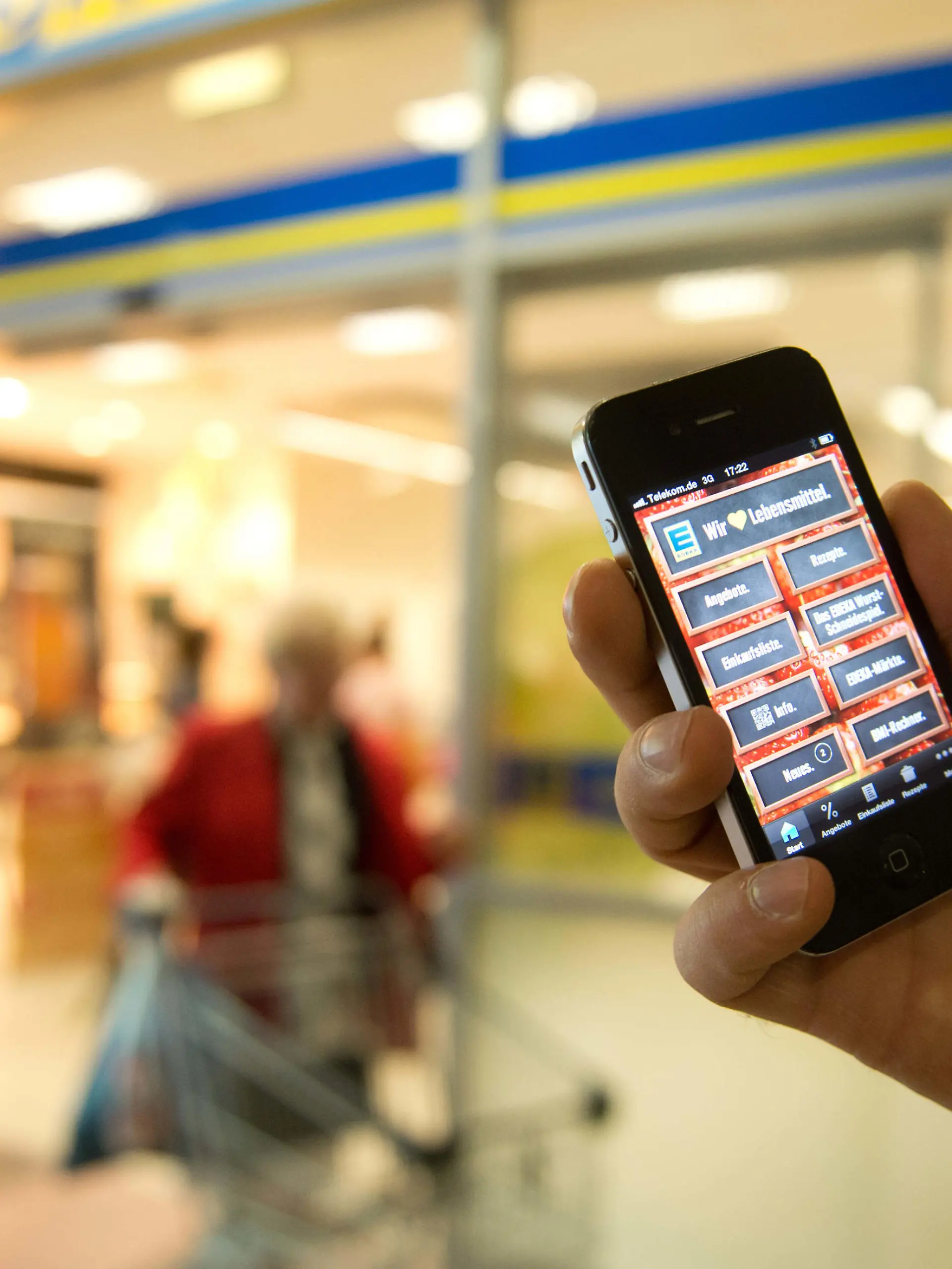 ILLUSTRATION - Ein Passant hält am 27.05.2013 in Berlin vor einem Edeka-Supermarkt ein Telefon mit der Edeka-App in die Kamera. Foto: Joanna Scheffel/dpa