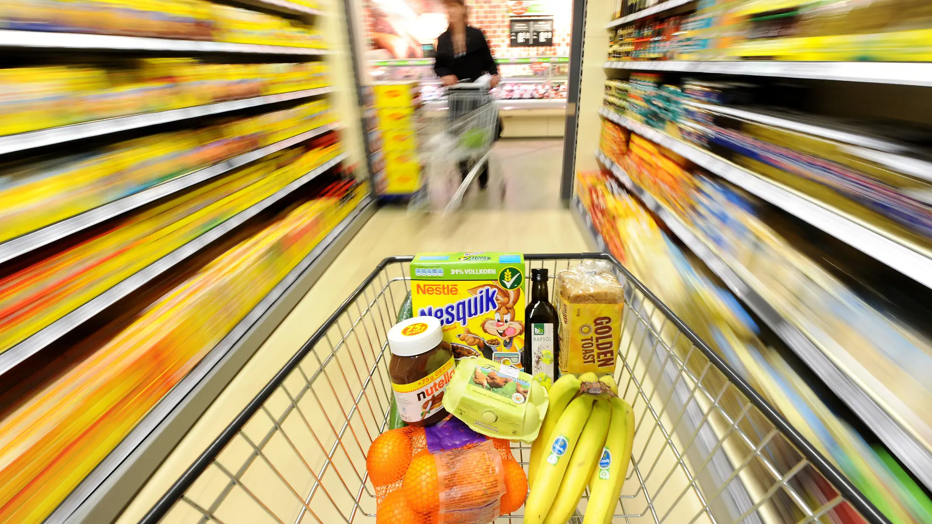 ARCHIV - ILLUSTRATION - Ein Einkaufswagen mit verschiedenen Lebensmitteln wie Eier, Bananen, Orangen, Nutella, Cornflakes, Rapsöl und Toastbrot wird am Montag (10.01.2011) durch einen Supermarkt in Mülheim (Ruhr) geschoben (Aufnahme mit langer Verschlusszeit). Auf die Verbraucher in Deutschland kommen abermals höhere Lebensmittelpreise zu. Landwirtschaft und Ernährungsindustrie kündigten am Mittwoch in Berlin Aufschläge von bis zu drei Prozent an. Damit wollen sie höhere Kosten für Löhne, Energie und Rohstoffe ausgleichen. Ob die Preise im Supermarkt ähnlich stark steigen, ist unklar. Im deutschen Lebensmittelmarkt herrscht ein scharfer Wettbewerb. Foto: Julian Stratenschulte dpa/lnw +++(c) dpa - Bildfunk+++