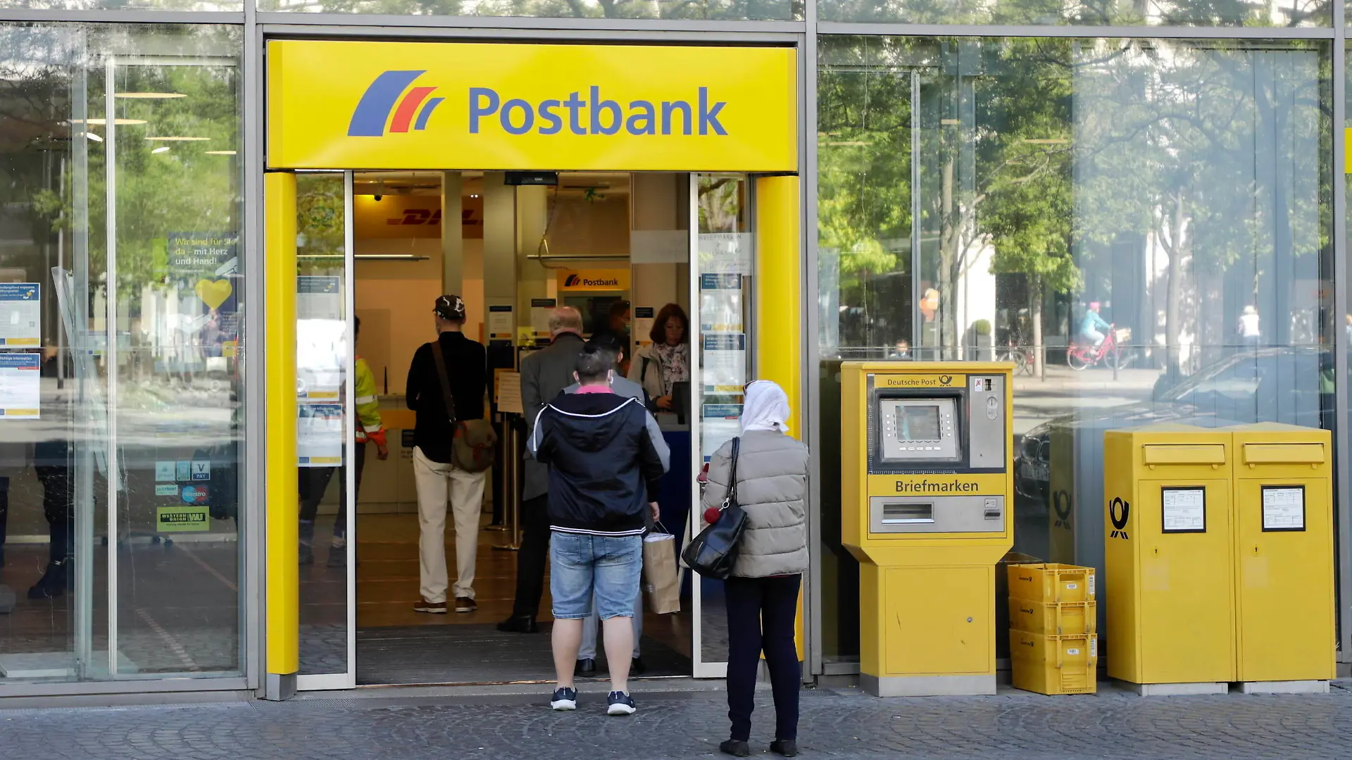 06.05.2020, Frankfurt am Main, Deutschland - Corona-Krise. Foto: Passanten mit Mundschutz stehen mit Mindestabstand in einer Warteschlange in einer Postbank-Filiale in der Innenstadt. *** 06 05 2020, Frankfurt am Main, Germany Corona Crisis Photo Passers-by with mouthguards stand with a minimum distance in a queue in a Postbank branch in the city centre