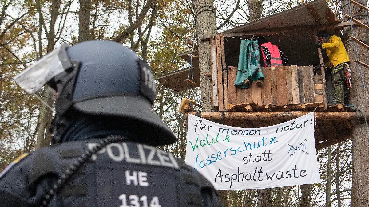 ARCHIV - 10.11.2020, Hessen, Niederklein: Ein Polizist steht im Dannenröder Forst vor einem Baumhaus, in dem sich Aktivisten aufhalten. Die Demonstranten protestierten gegen weitere Rodungsarbeiten für den Weiterbau der Autobahn 49.     (zu dpa «Land zahlt Polizei mit knapp 15 Millionen Euro Überstunden aus») Foto: Helmut Fricke/dpa +++ dpa-Bildfunk +++