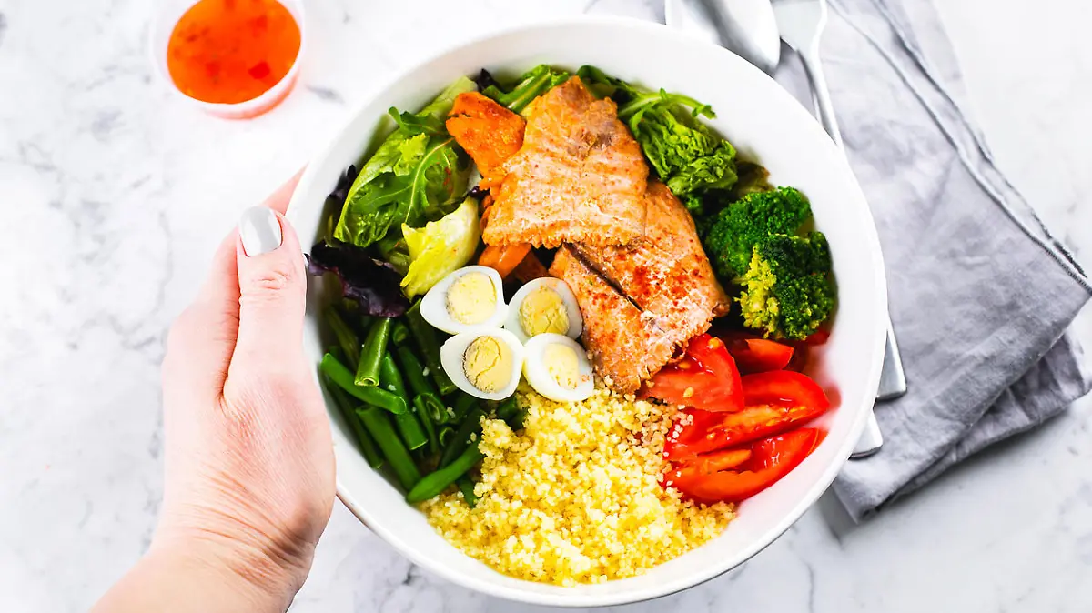 Healthy meal, keto food concept. Fish salad bowl on marble table background. Salad with salmon, couscous, vegetables, quail eggs. Top view, copy space