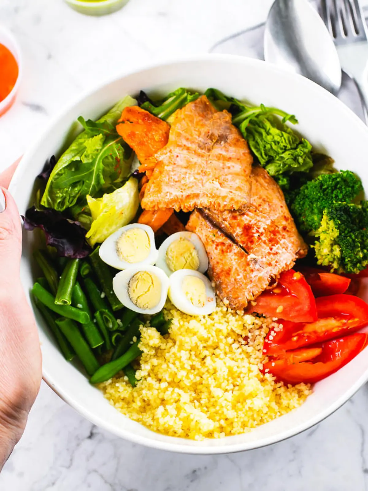 Healthy meal, keto food concept. Fish salad bowl on marble table background. Salad with salmon, couscous, vegetables, quail eggs. Top view, copy space