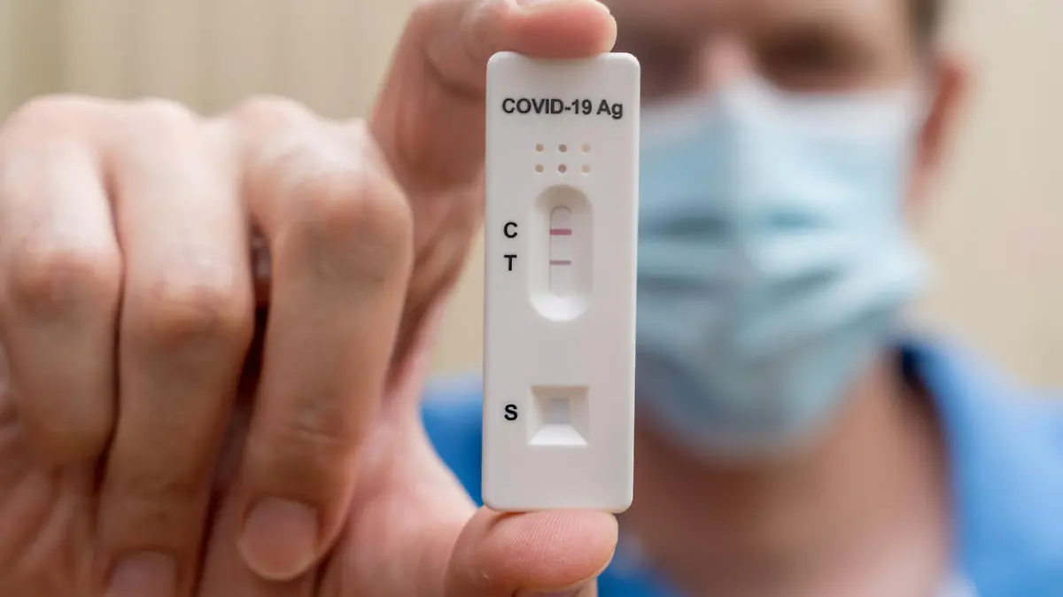 Man wearing face mask holding Covid-19 rapid antigen test cassette with negative result of rapid diagnostic test. Self-testing kit at home