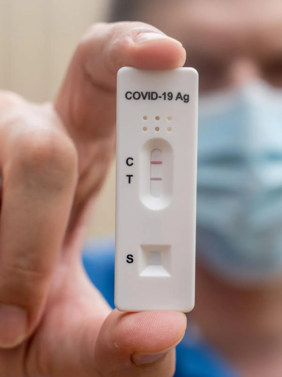 Man wearing face mask holding Covid-19 rapid antigen test cassette with negative result of rapid diagnostic test. Self-testing kit at home