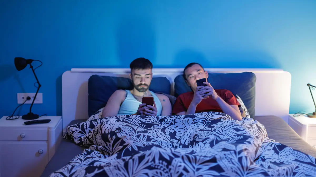 Homosexual couple using smart phones in bed and ignoring each other