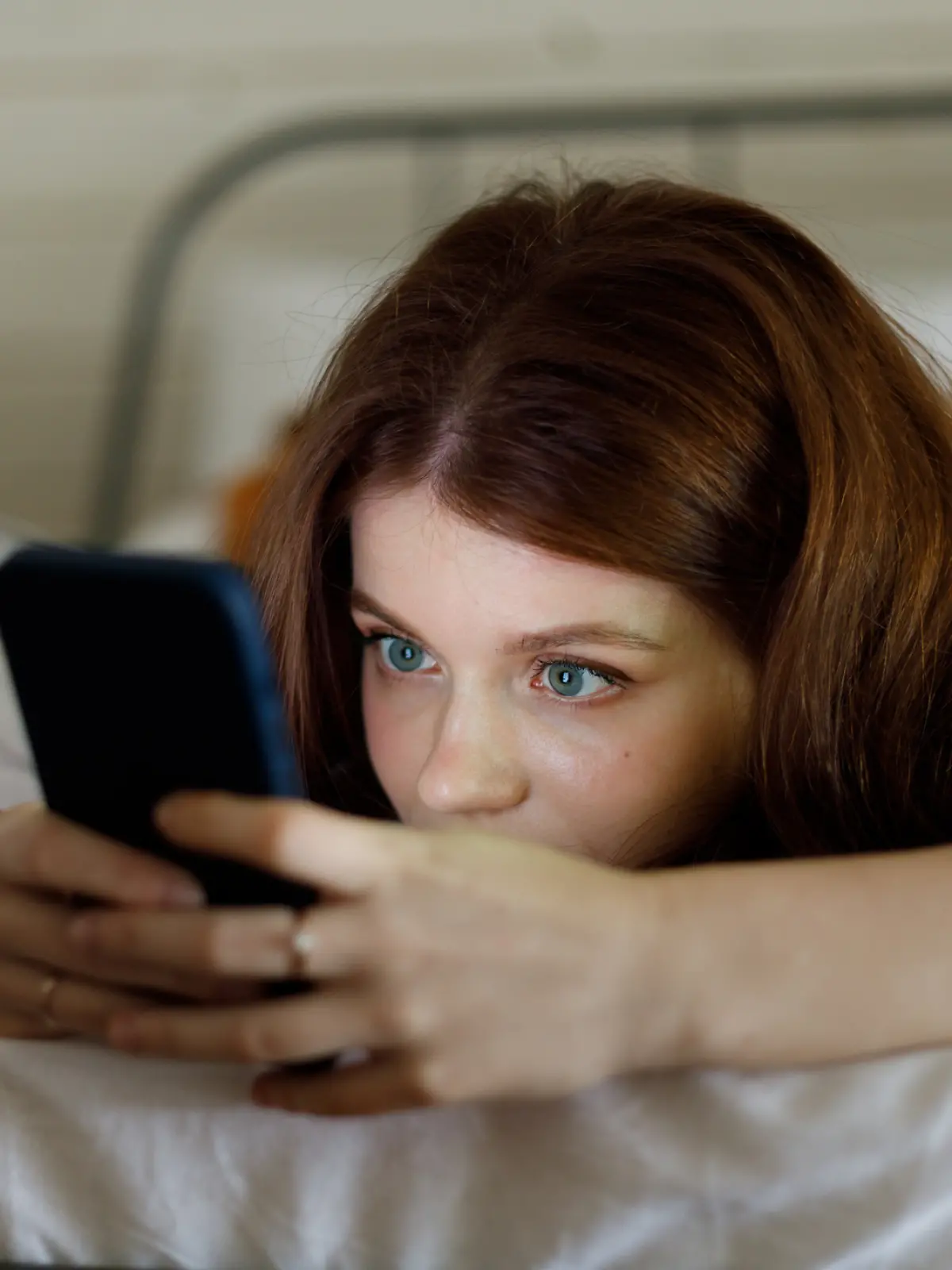 Eine junge Frau liegt auf dem Bett und surft am Handy.