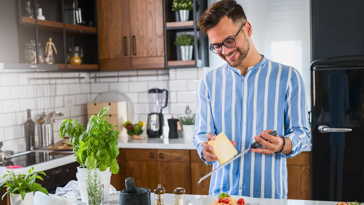 Ein Mann reibt mit einer Käsereibe Käse über seine Pasta.