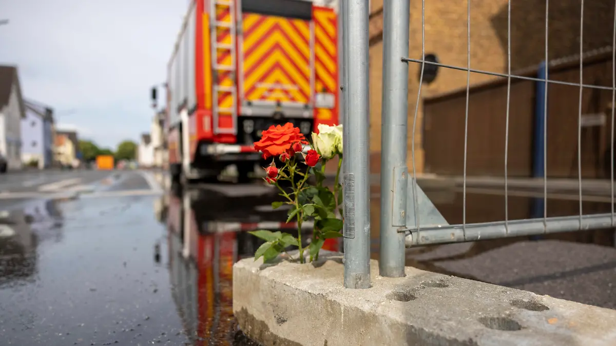 19.06.2023, Nordrhein-Westfalen, Sankt Augustin: Blumen stehen an dem Absperrgitter in der Straße in Sankt Augustin, wo am Sonntag ein Motorradgeschäft brannte. Nach dem Brand mit zwei toten Feuerwehrleuten laufen die Ermittlungen zur Brandursache. Foto: Thomas Banneyer/dpa +++ dpa-Bildfunk +++