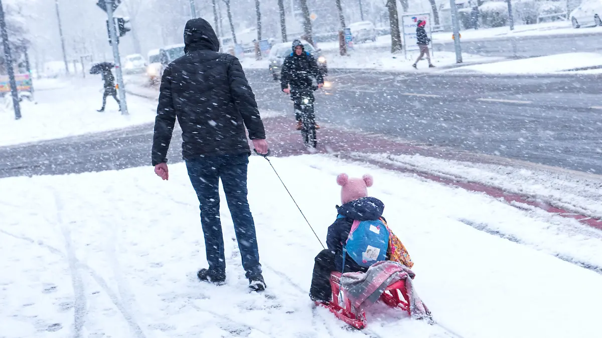 31.03.2022, Hamburg: Ein Mann zieht bei Schneefall seine Tochter auf einem Schlitten zur Kindertagesstätte. Foto: Daniel Bockwoldt/dpa +++ dpa-Bildfunk +++