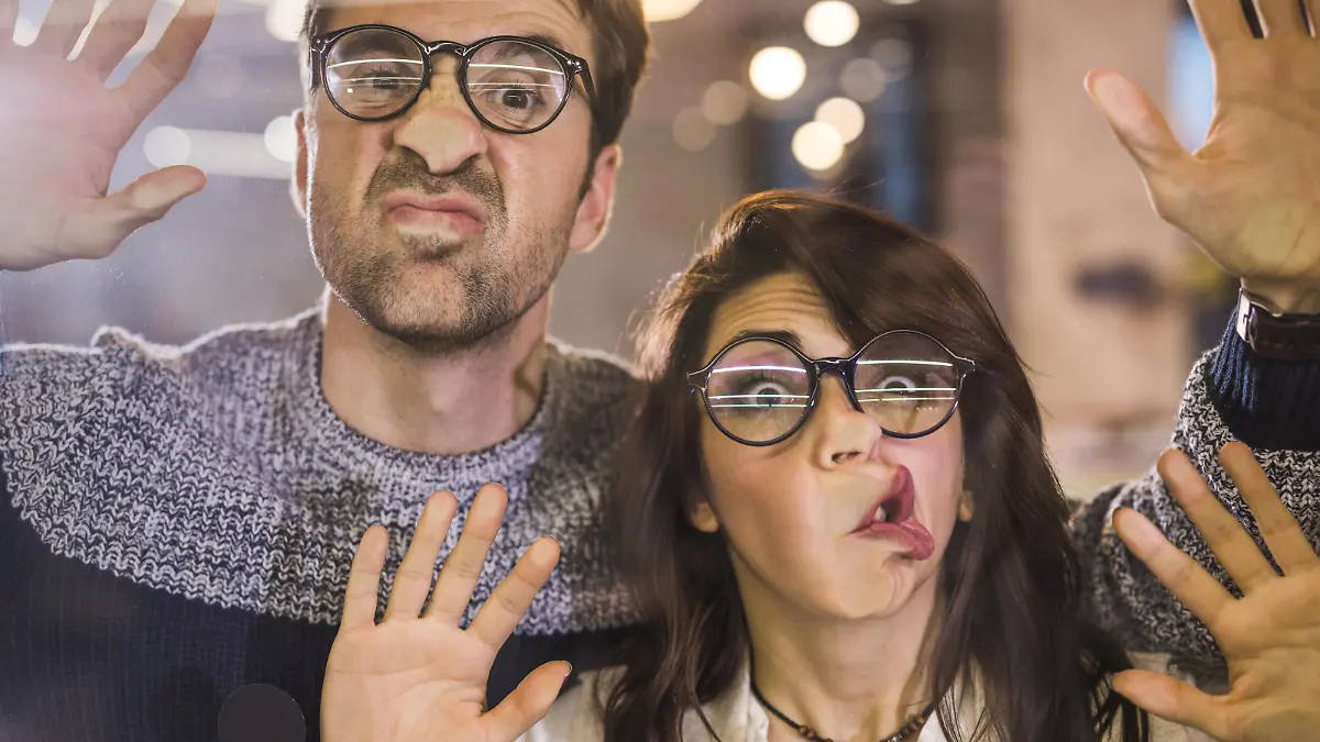 Young playful entrepreneurs making faces while playing with glass wall and looking at camera. The view is through glass.