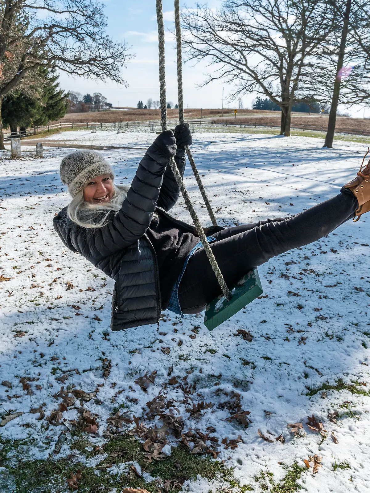 Smiling woman on swing in snow, Laechelnde Frau auf Schwingen im Schnee || Modellfreigabe vorhanden
