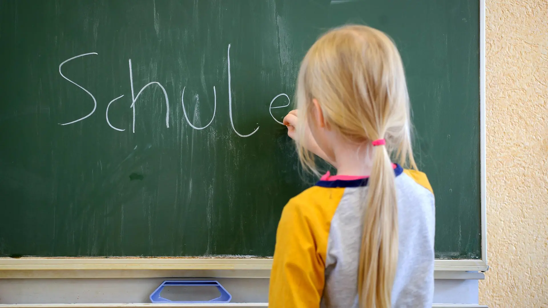Ein Schulkind schreibt mit Kreide an eine Schultafel den Satz Schule ist schön , aufgenommen am 19.01.2015 in Dresden.