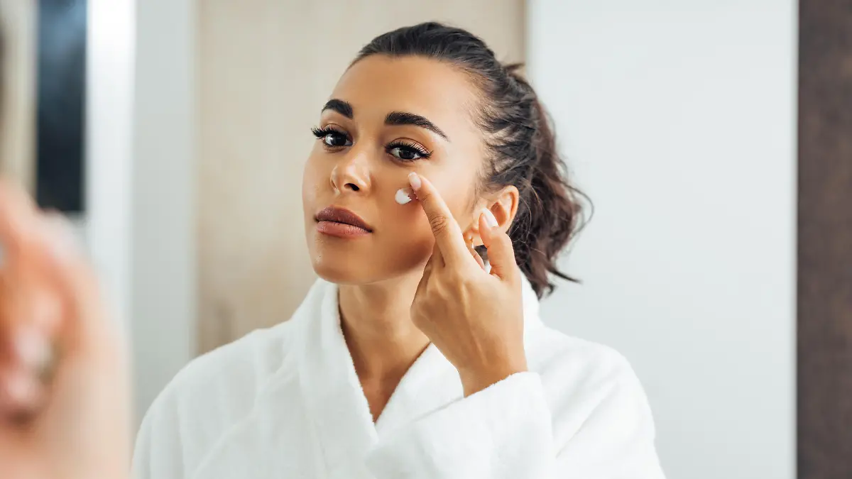 Beautiful woman in bathrobe applying anti-aging cream on her cheek