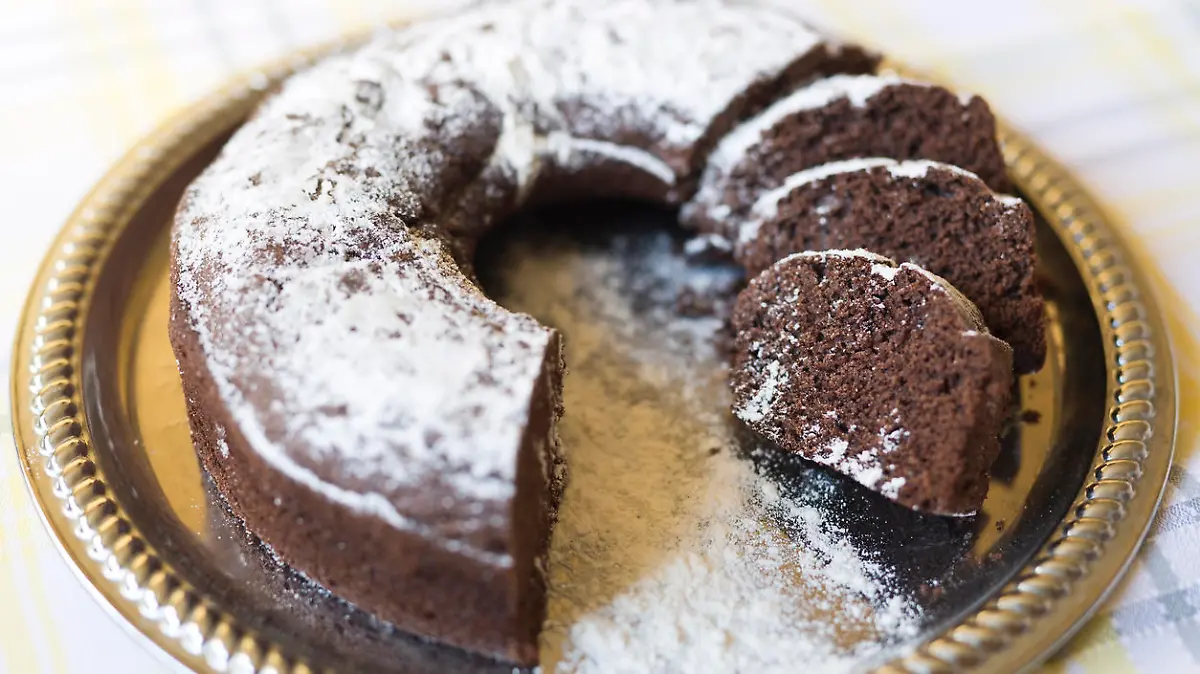 Homemade chocolate cake, with sugar glass on top, on a golden tray. Horizontal shot with natural light from a window.