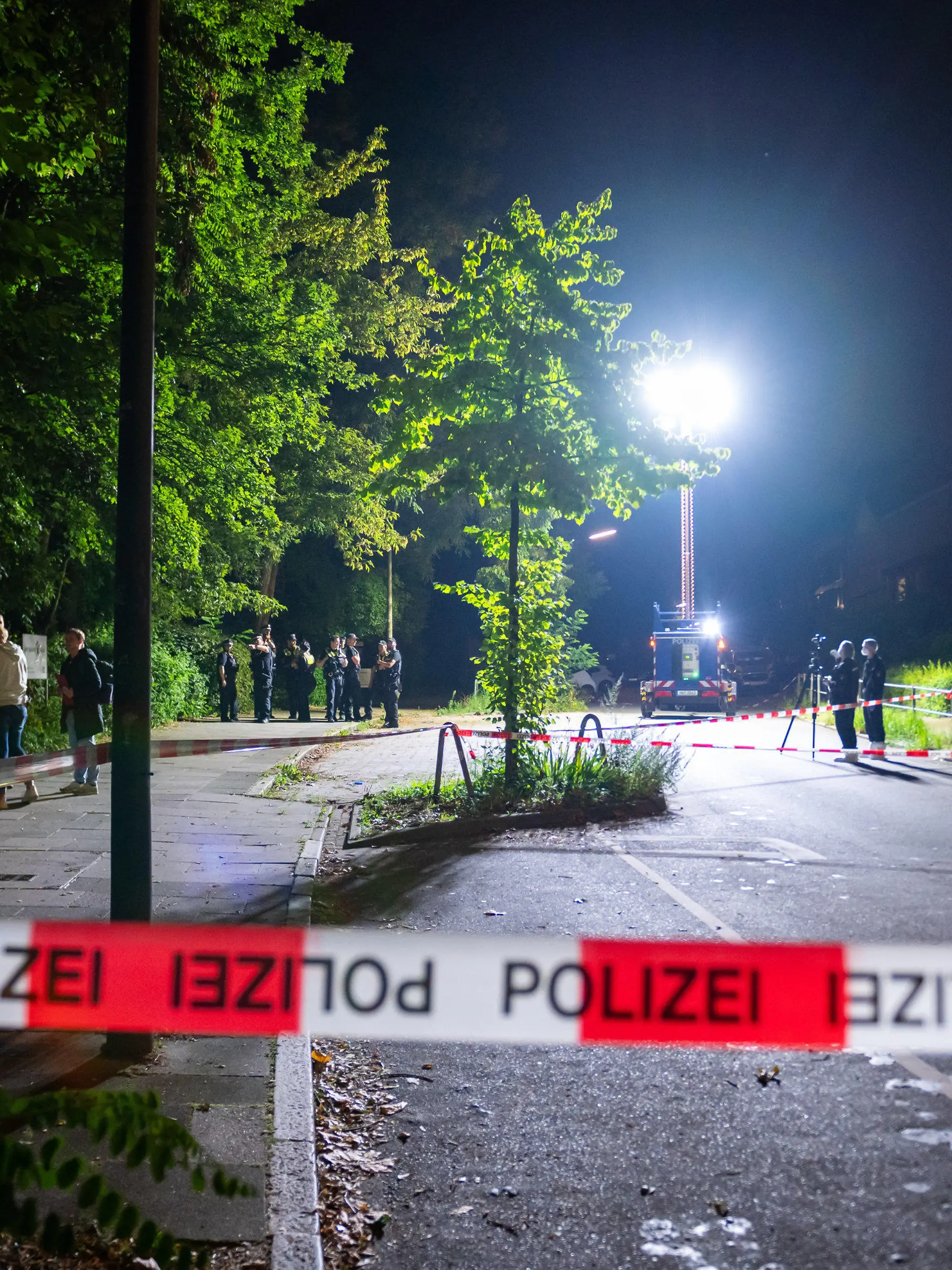 26.08.2023, Hamburg: Ein Lichtmast erhellt den abgesperrten Tatort während Kriminaltechniker mit einem 3D-Scanner arbeiten und weitere Polizeibeamte ermitteln. Im Hamburger Stadtteil Borgfelde ist ein Mann auf offener Straße von mehreren Schüssen getroffen worden. Er erlag seinen Verletzungen im Krankenhaus, wie die Polizei am Samstagmorgen mitteilte. Der Täter sei auf der Flucht, eine Fahndung eingeleitet worden. Foto: Jonas Walzberg/dpa +++ dpa-Bildfunk +++