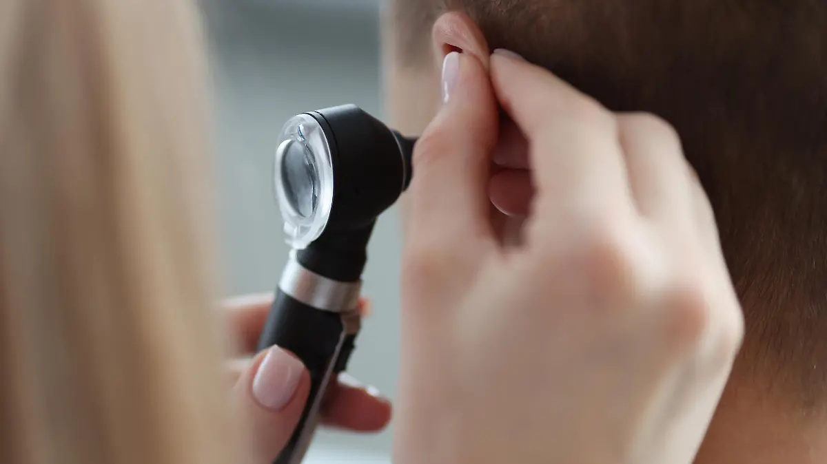 Otorhinolaryngologist pulling ear with his hand and looking at it with otoscope closeup. Otoscopy concept