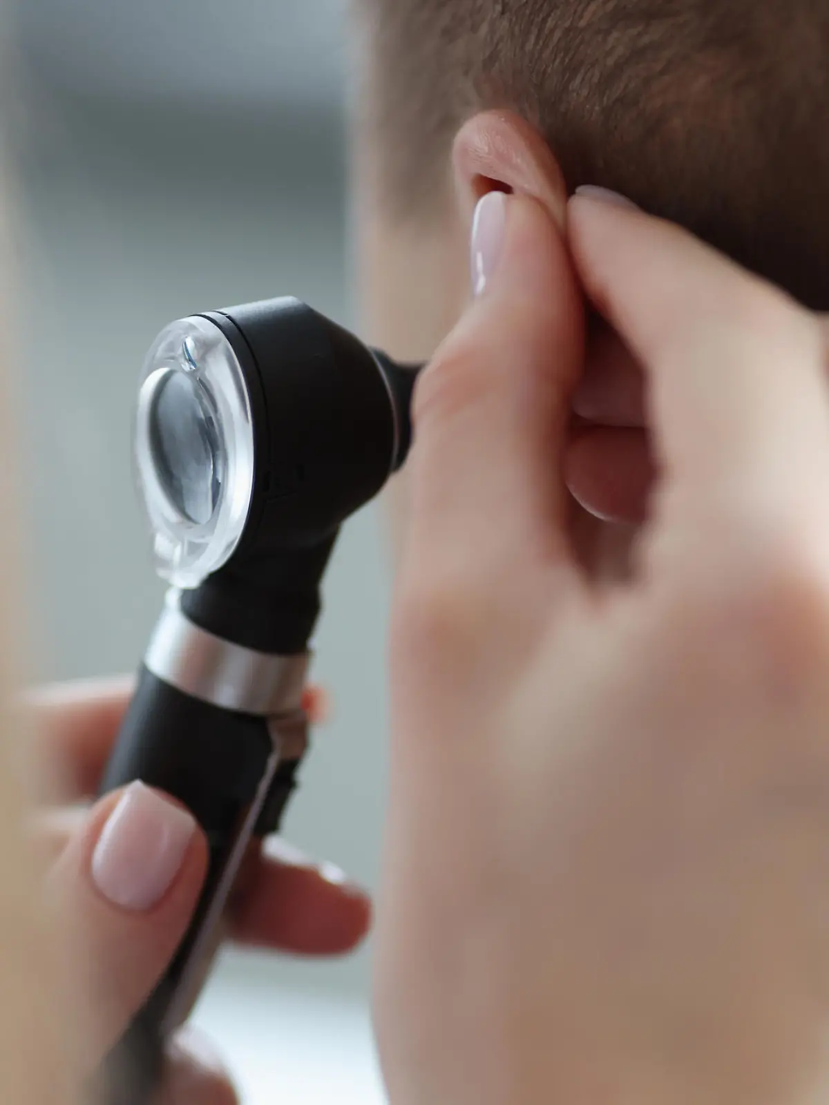 Otorhinolaryngologist pulling ear with his hand and looking at it with otoscope closeup. Otoscopy concept