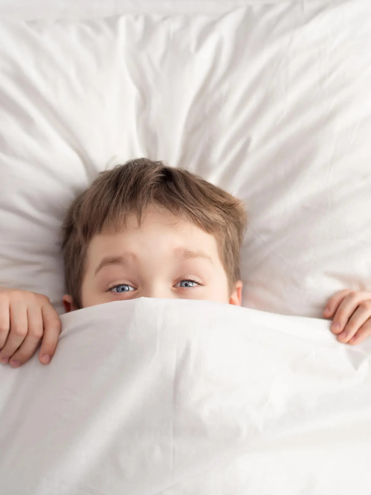Cheerful boy in white bed under white blanket. Sleeping boy. Sleeping child