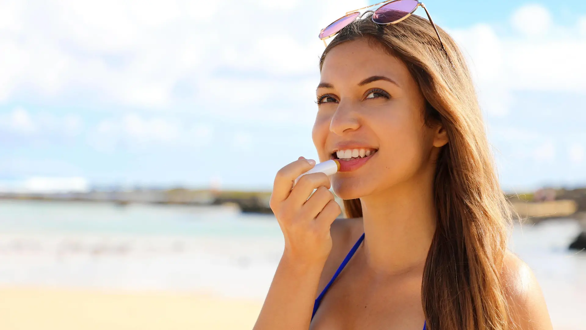 Smiling young woman applying sun protection on her lip on the beach. Attractive young woman putting lip balm on lips. Copyright: xsergiomontix Panthermedia28070927 ,model released, Symbolfoto