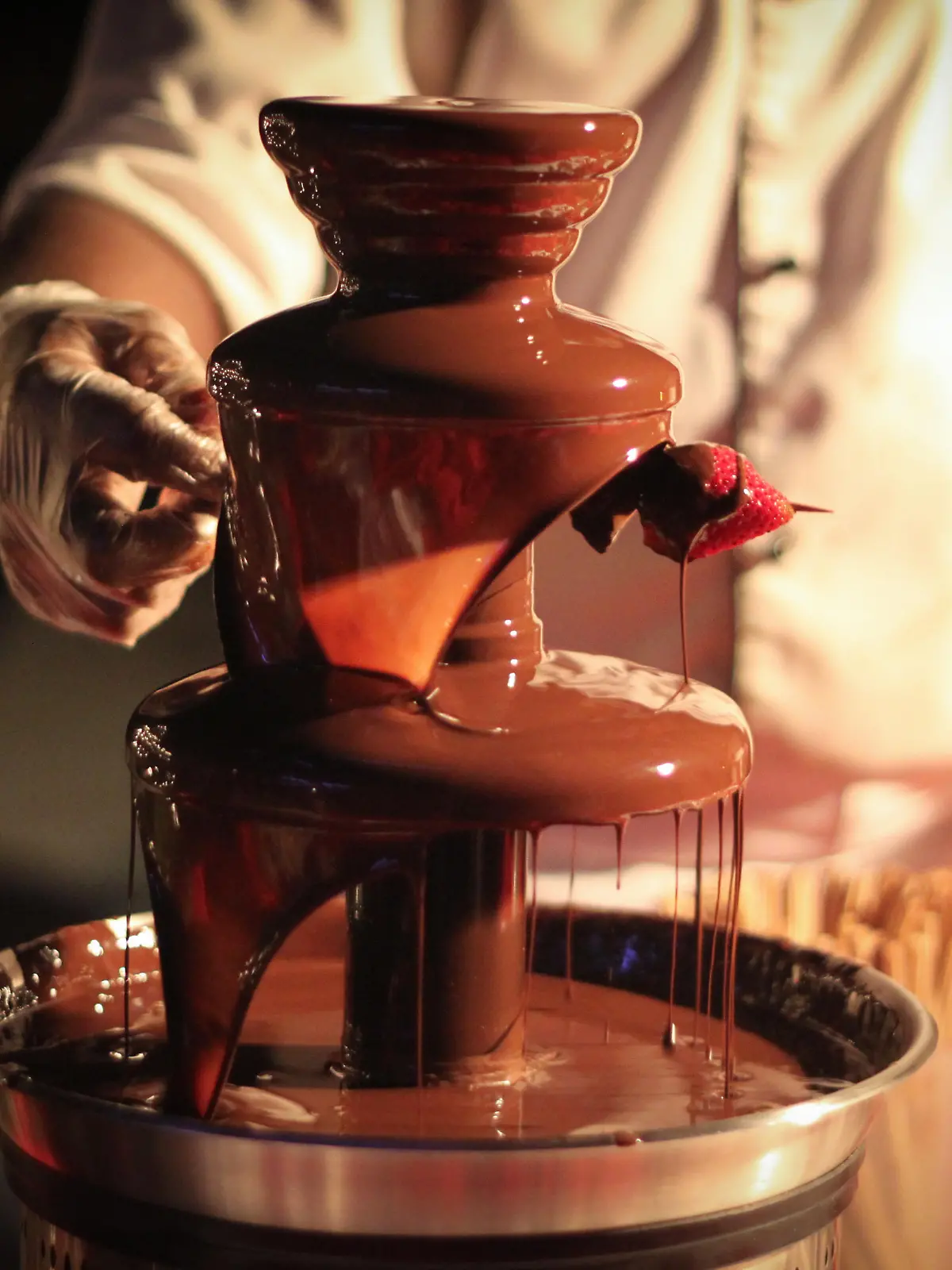 Chef is preparing a strawberry skewer under a chocolate fountain/ Schokoladenbrunnen