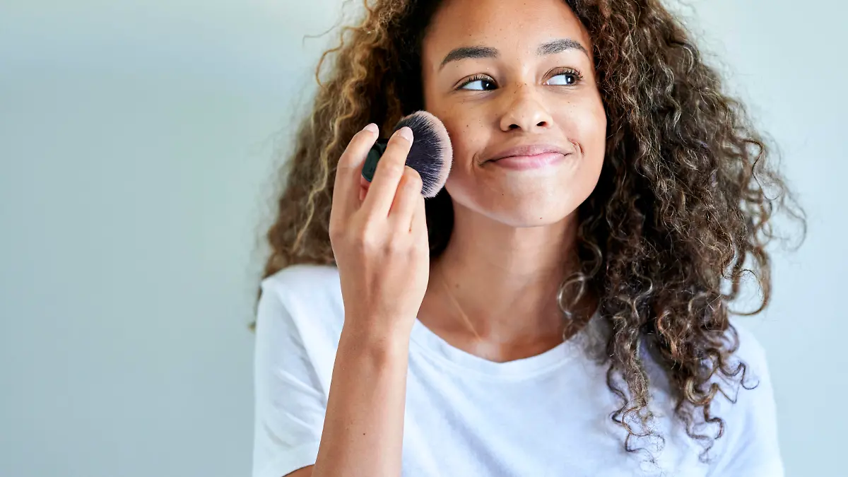 Smiling young woman applying face powder with make-up brush against white wall model released Symbolfoto KIJF03507 