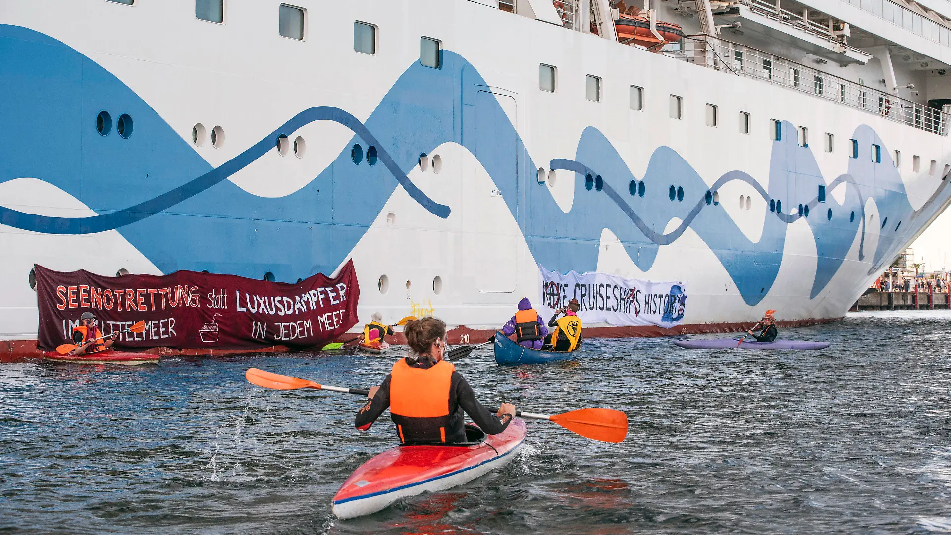17.06.2023, Mecklenburg-Vorpommern, Rostock-Warnemünde: Klimaaktivisten versuchen auf Kanus und aufblasbaren Booten das Kreuzfahrtschiff «Aida Diva» am Auslaufen zu hindern. Die Aktivisten haben eine Aktion gegen den Kreuzfahrttourismus gestartet. Foto: Frank Hormann/dpa +++ dpa-Bildfunk +++