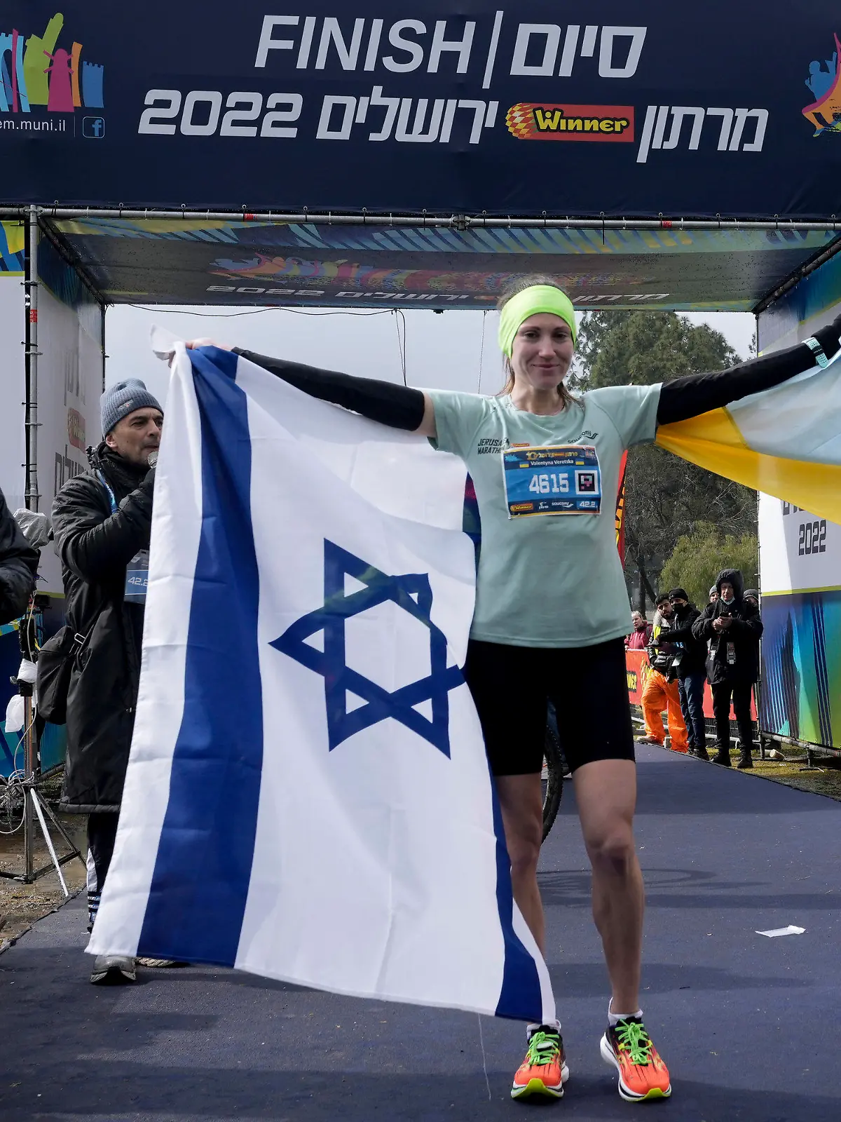 25.03.2022, Israel, Jerusalem: Valentyna Veretska, Läuferin aus der Ukraine, steht mit der ukrainischen und der israelischen Fahne, nachdem sie den ersten Platz bei den Frauen im Jerusalem-Marathon gewonnen hat. Die 31-jährige Veretska nahm an dem Rennen teil, nachdem sie mit ihrer 11-jährigen Tochter kurz nach dem Einmarsch Russlands in die Ukraine am 24. Februar geflohen war. Foto: Mahmoud Illean/AP/dpa +++ dpa-Bildfunk +++