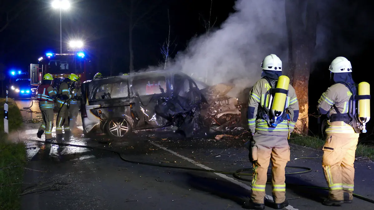 26.03.2022, Siegburg: Die Feuerwehr steht vor dem Wrack eines ausgebrannten Autos, in dem zwei Menschen ums Leben gekommen sind. Laut Polizei waren drei junge Männer in einem Lieferwagen in einer Kurve von der Straße abgekommen und gegen einen Baum geprallt. Der Wagen sei zurückgeschleudert und in Brand geraten, sagte der Sprecher. Die Getöteten seien junge Männer aus Siegburg des Jahrgangs 2005, sagte der Sprecher. Foto: Christof Schmoll/dpa +++ dpa-Bildfunk +++