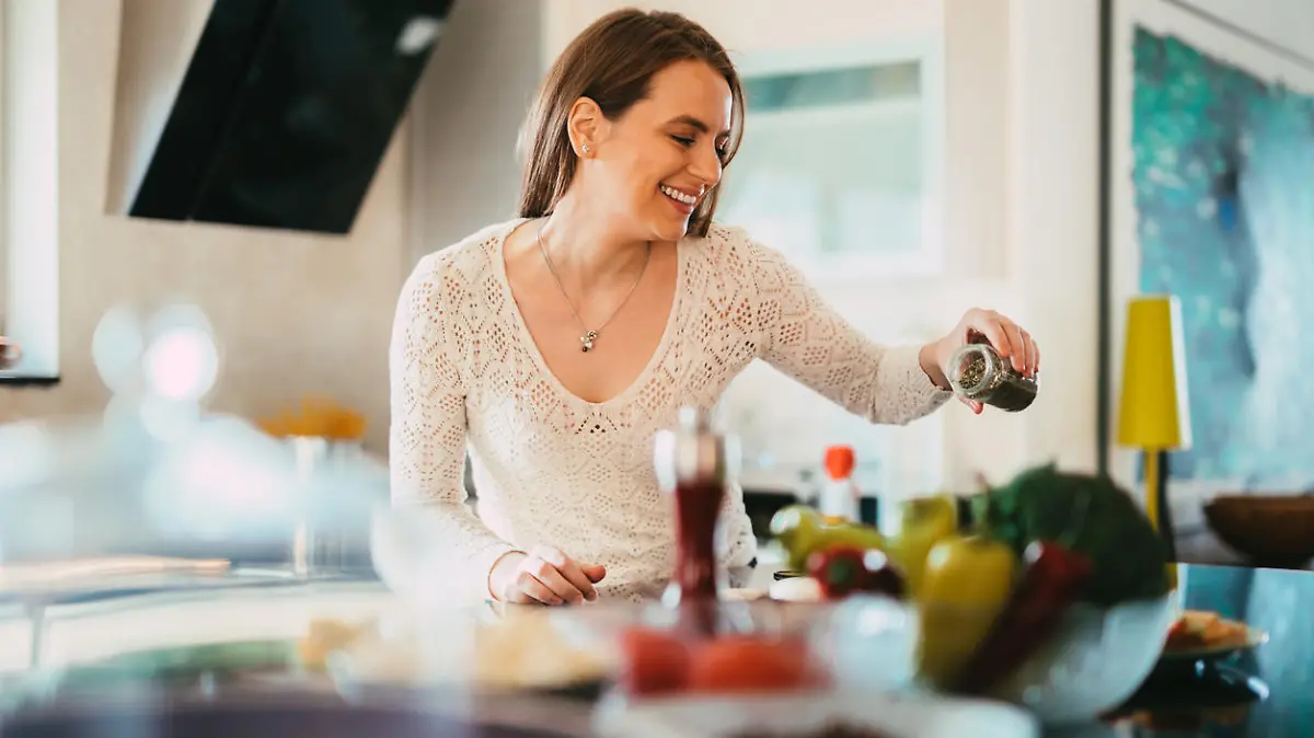 Beautiful young casually dressed woman preparing healthy food and seasoning salad in the kitchen at home