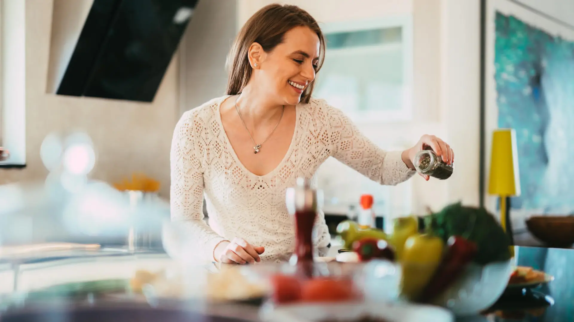 Beautiful young casually dressed woman preparing healthy food and seasoning salad in the kitchen at home
