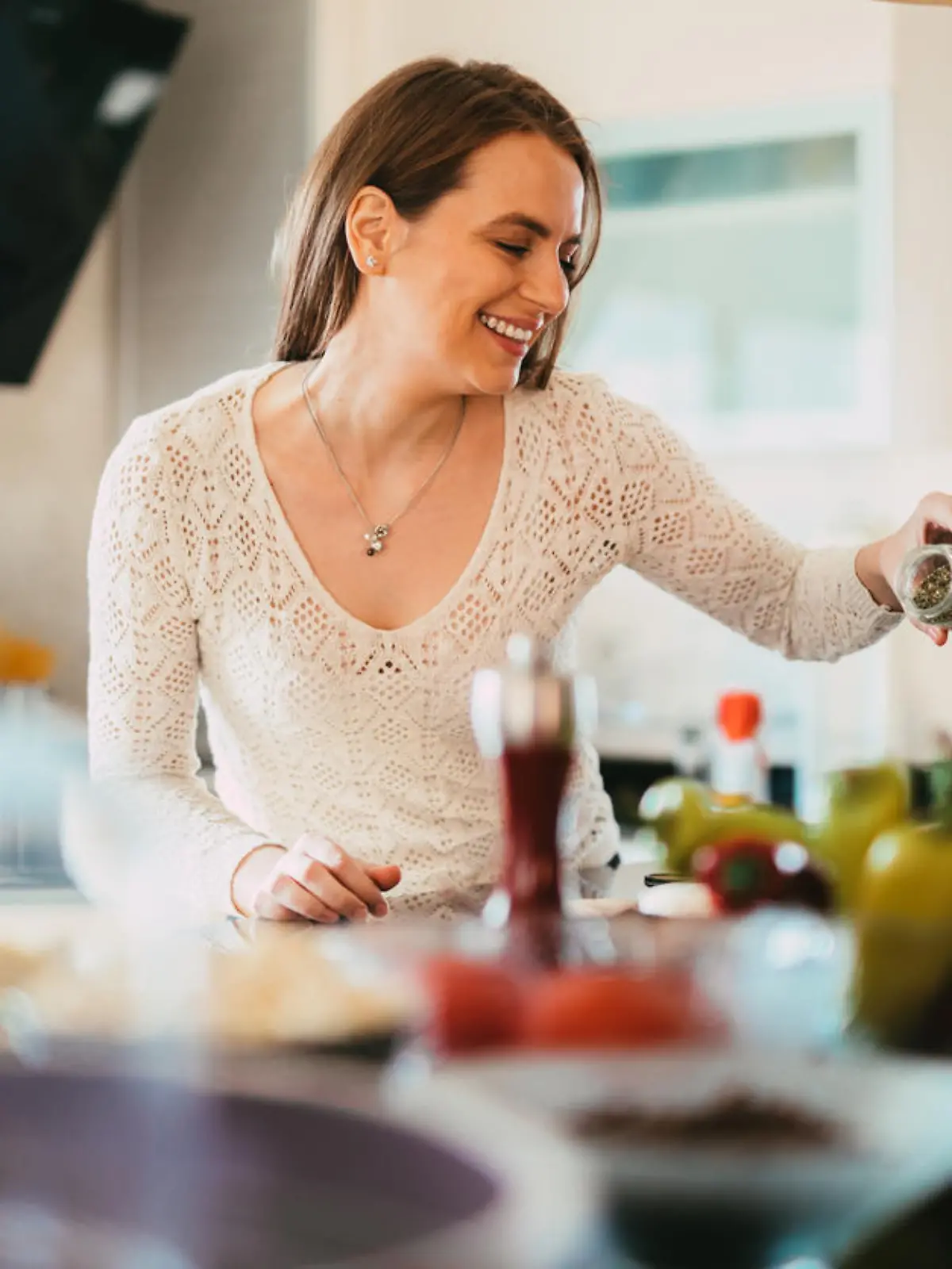 Beautiful young casually dressed woman preparing healthy food and seasoning salad in the kitchen at home