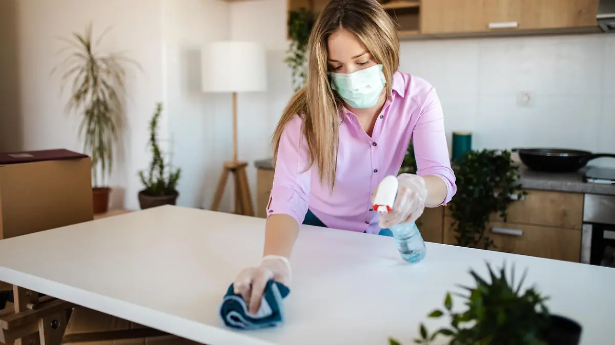 Young woman wearing mask for protection of COVID-19 pandemic while disinfecting her new house
