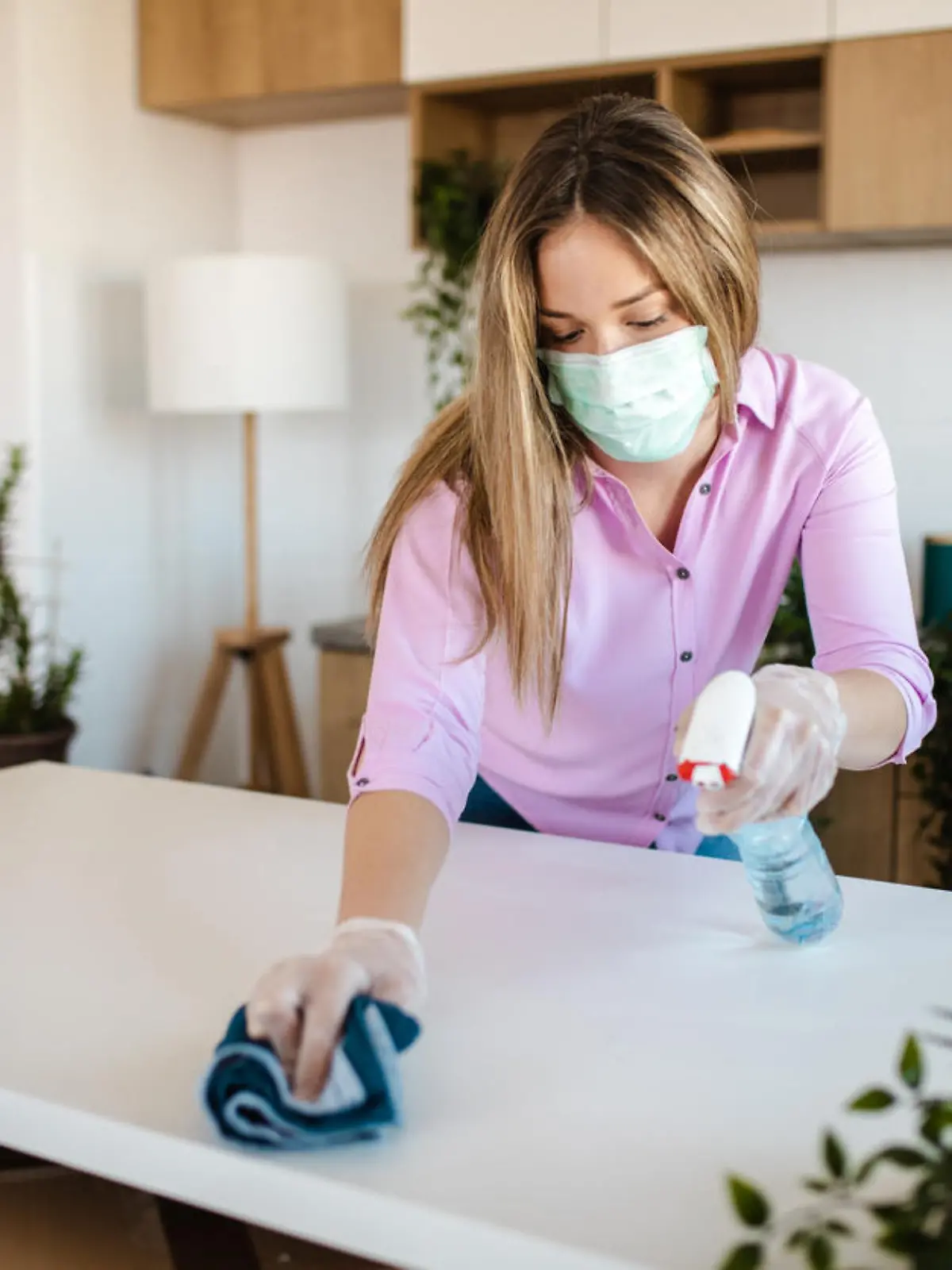 Young woman wearing mask for protection of COVID-19 pandemic while disinfecting her new house