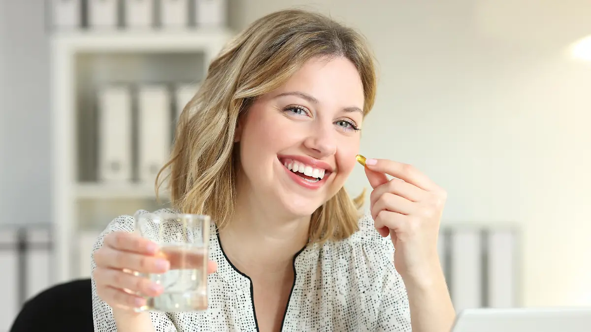 Happy office worker showing a vitamin supplement pill and a water glass looking at camera