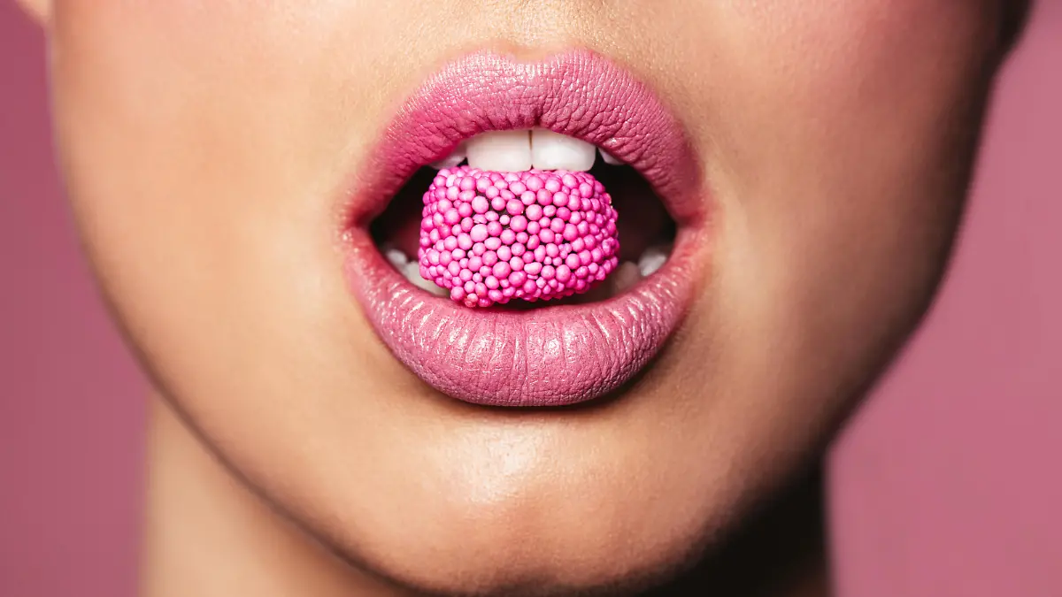 Beautiful pink lips with a piece of sweet candy. Close up of young woman with candy in mouth.