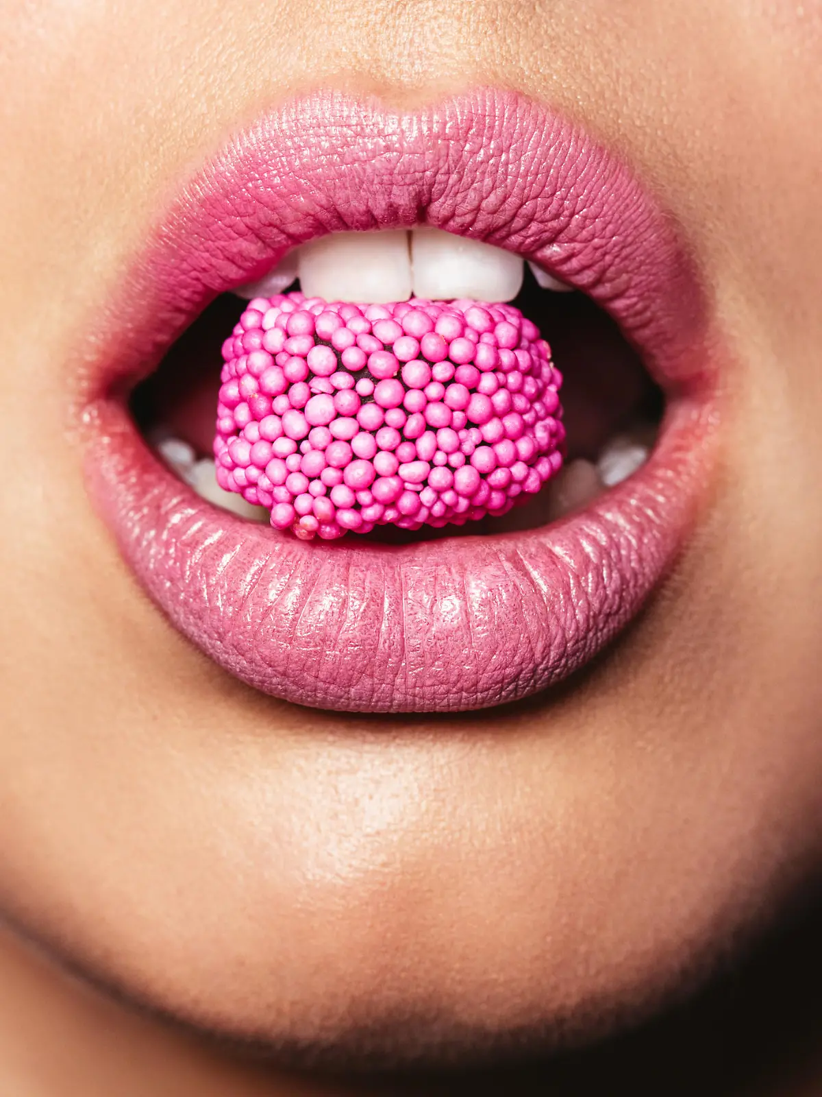 Beautiful pink lips with a piece of sweet candy. Close up of young woman with candy in mouth.
